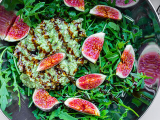 Fig salad with soft cheese and blueberries, avocado, arugula, balsamic sauce in steel bowl. Food...