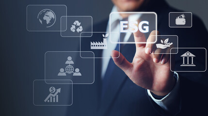 Businessman touching button ESG on-screen with connected virtual icons over the background.ESG environmental social governance business strategy investing concept.