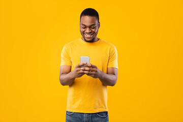 Smiling Black Man Using Smartphone Browsing Internet Over Yellow Background