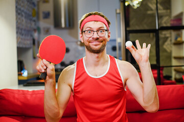 Funny crazy athlete nerd with ping pong table tennis racket and ball at home.