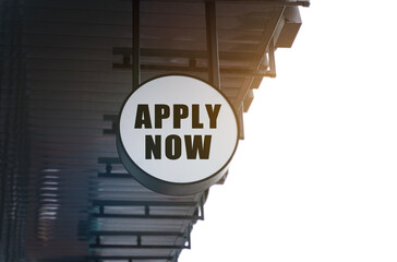 There is a circular sign under the roof of the building that says - APPLY NOW