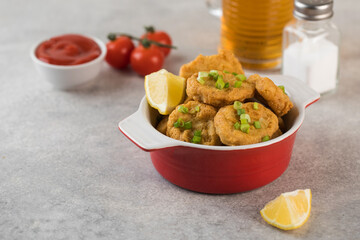 Golden chicken nuggets in a red bowl, sprinkled with green onions and a lemon wedge. Pub menu