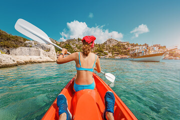 Happy girl is rowing on a double sea kayak with her friend near Kekova island with view of Simena Castle and Kaleucagiz village in Turkey. Outdoor recreation and exploration. Travel as a lifestyle