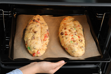 Woman putting baking tray with raw homemade Stollens into oven, closeup. Traditional German...