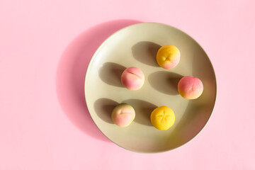 Marzipan fruits in the plate on pink pastel background. Martorana fruit molded a shape of peaches. Typical sicilian pastries - frutta Martorana.