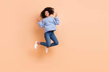 Fototapeta na wymiar Full length body size view of attractive trendy cheery funny girl jumping showing v-sign isolated over beige pastel color background
