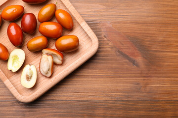 Wooden plate with fresh Ziziphus jujuba fruits on table, top view. Space for text