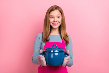 Portrait of attractive cheerful girl wearing apron cooking homemade soup isolated over pink pastel...