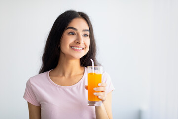 Cheerful Indian woman holding glass of refreshing fruit juice indoors. Summer detox, wellness, dieting concept