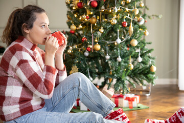 Young woman drinking coffee by the Christmas tree.