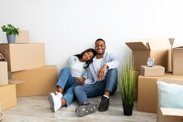 Real estate rent concept. Loving african american spouses relocating to new apartment, sitting among cardboard boxes