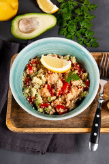  Salmon salad with tomatoes, avocado and quinoa in a blue bowl on a dark gray table vertical photo, a dish of balanced diet