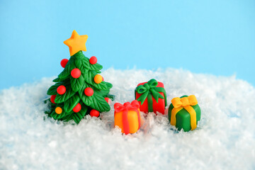 Plasticine figures of Christmas tree and gifts on a white artificial snow. Happy New Year card