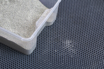A litter box with clumping litter sits on a honeycomb EVA mat. Small filler particles from the feet...