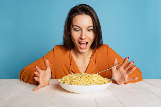 Shocked young girl preparing to eat large portion of noodles isolated on blue studio background. World pasta day