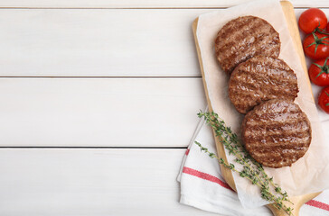 Tasty grilled hamburger patties, cherry tomatoes and thyme on white wooden table, flat lay. Space...