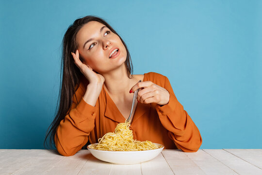 Romantic young girl dreaming about taste of delicious Italian pasta isolated on blue studio background. World pasta day
