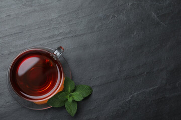 Cup of hot aromatic tea with mint on black table, flat lay. Space for text