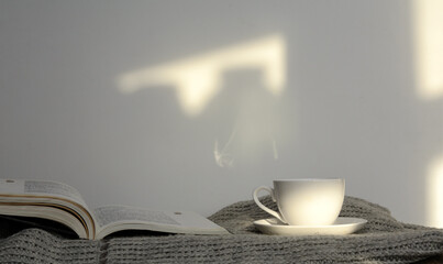 An open book lies on a knitted sweater. Next to a cup of coffee. White background. Concept - morning coffee