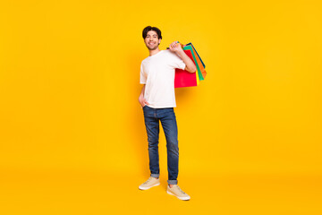 Full length body size view of attractive cheerful guy carrying new things buyings isolated over bright yellow color background