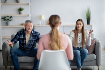 Mature couple having argument at psychologist's office, matiral counselor sitting with back to camera