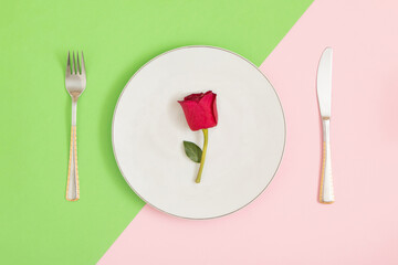 On a colorful table, pastel colors, neatly arranged knife, fork and plate. A red rose was served for the meal. Romantic dinner. Valentine's Day.
