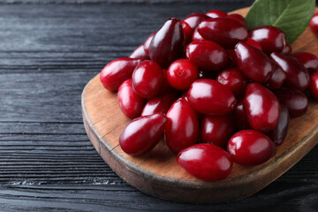 Fresh ripe dogwood berries with green leaf on black wooden table, closeup