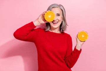 Portrait of nice cheerful grey-haired woman holding orange piece closing eye having fun isolated over pink pastel color background