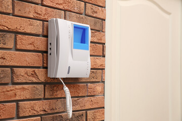 Modern intercom system with handset on red brick wall indoors, space for text