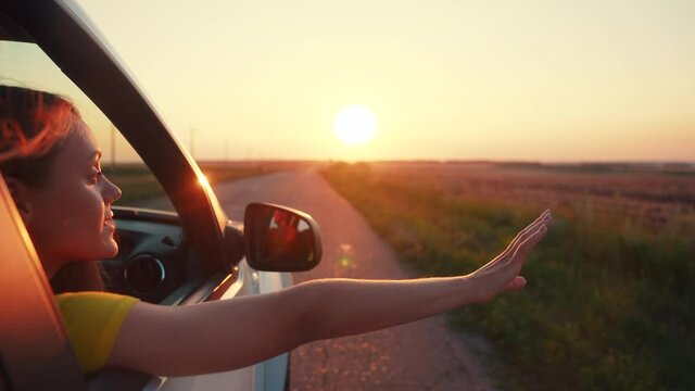 travel by car concept. the girl put her hand in the car window at sunset. freedom road a drive concept. sun girl travel by car goes on vacation on the road at sunset. summer adventure