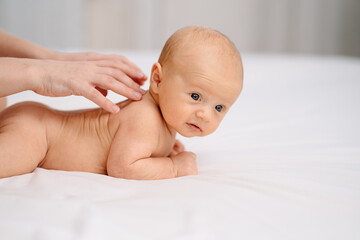 the baby lies on his tummy on a white sheet. and mom's hands massage the back. 