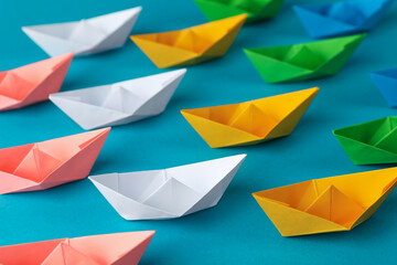 Many colorful handmade paper boats on light blue background. Origami art