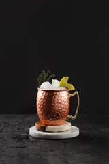 Fototapete Moskau Traditional american alcoholic beverage moscow mule in copper mug with lemon and thyme on white marble boards, black background