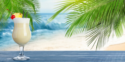 Tasty Pina Colada cocktail on wooden table near ocean, space for text. Banner design