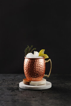 Traditional american alcoholic beverage moscow mule in copper mug with lemon and thyme on white marble boards, black background