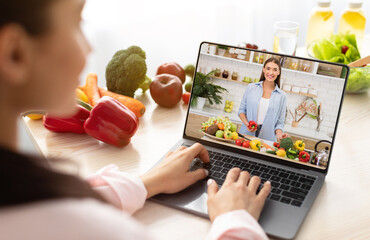 Young woman using laptop computer to take part in online culinary workshop, learning vegan cuisine recipes on web