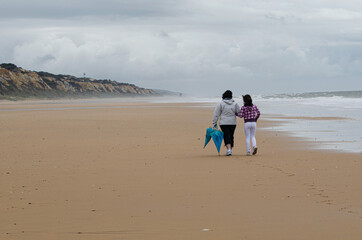 Paeando por la playa madre e hija con paraguas en un dia frio