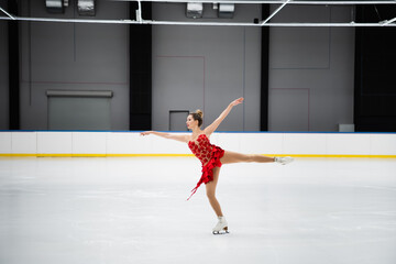 full length of figure skater in red dress performing camel spin in professional ice arena - obrazy, fototapety, plakaty