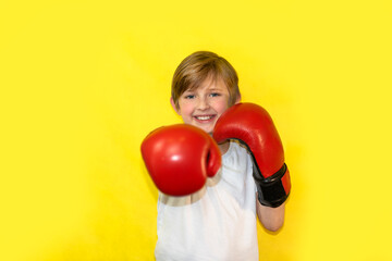 little boxer makes a blow to the camera. happy child in red boxing gloves stands on yellow...