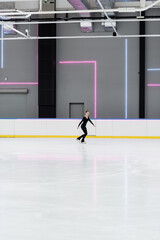 full length of figure skater in black bodysuit skating in professional ice arena