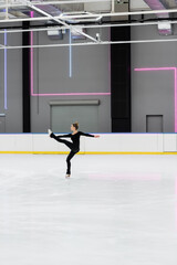 Fototapeta na wymiar full length of figure skater in black bodysuit practicing in professional ice arena