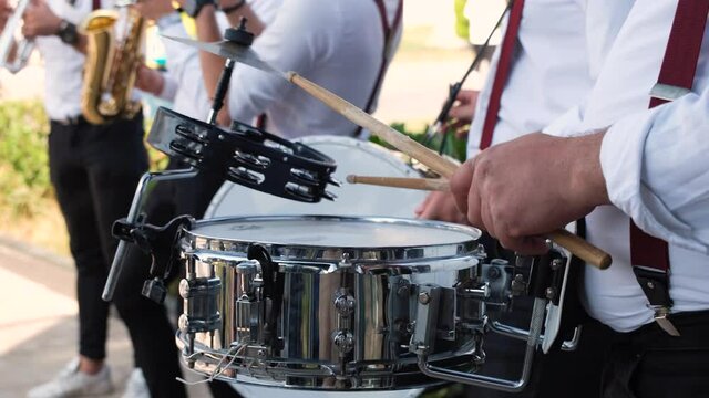 The person playing the snare drum. Music group playing musical instruments. People playing musical instruments outdoors.
