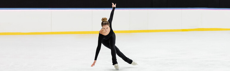 full length of professional figure skater in black bodysuit skating with outstretched hands in ice...