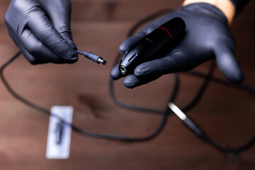 the hands of a permanent makeup artist in black medical gloves inserts a power cord into a tattoo...