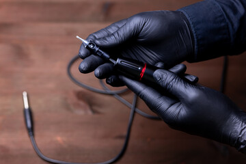 the hands of the permanent makeup master in black medical gloves are placed in a disposable cartridge in a tattoo machine - obrazy, fototapety, plakaty