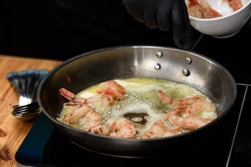 Fried red shrimps with garlic in olive oil on black pan on stove.