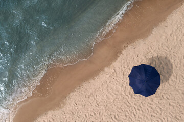Beach umbrella on sandy coast near sea, top view