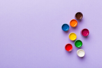 jars with gouache of different colors on Colored background. hobby painting. Top view with empty...