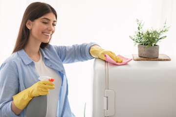 Cheerful young housewife cleaning dining table at kitchen