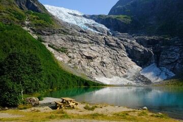 Fototapeta na wymiar Boyabreen Glacier and a glacial lake Jostedalsbreen National Park in Norway. Wooden benches are standing on bank of lake.